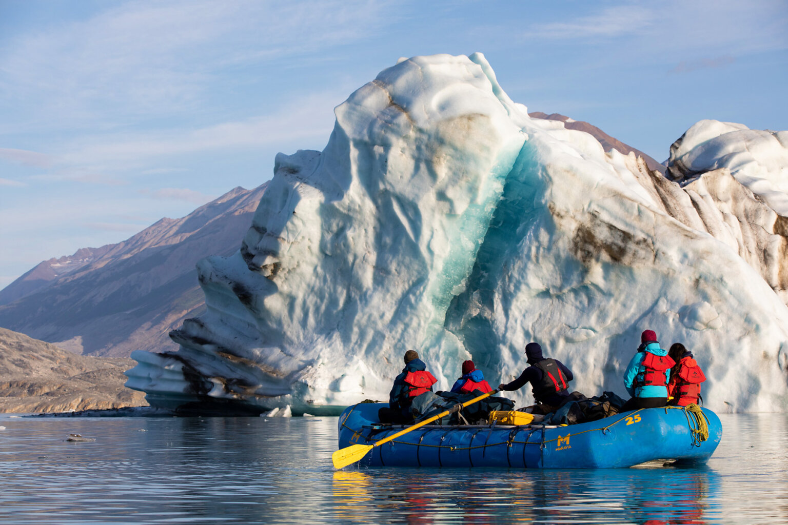 A raft with four guests and a guide row by a giant glacier on the Alsek River.