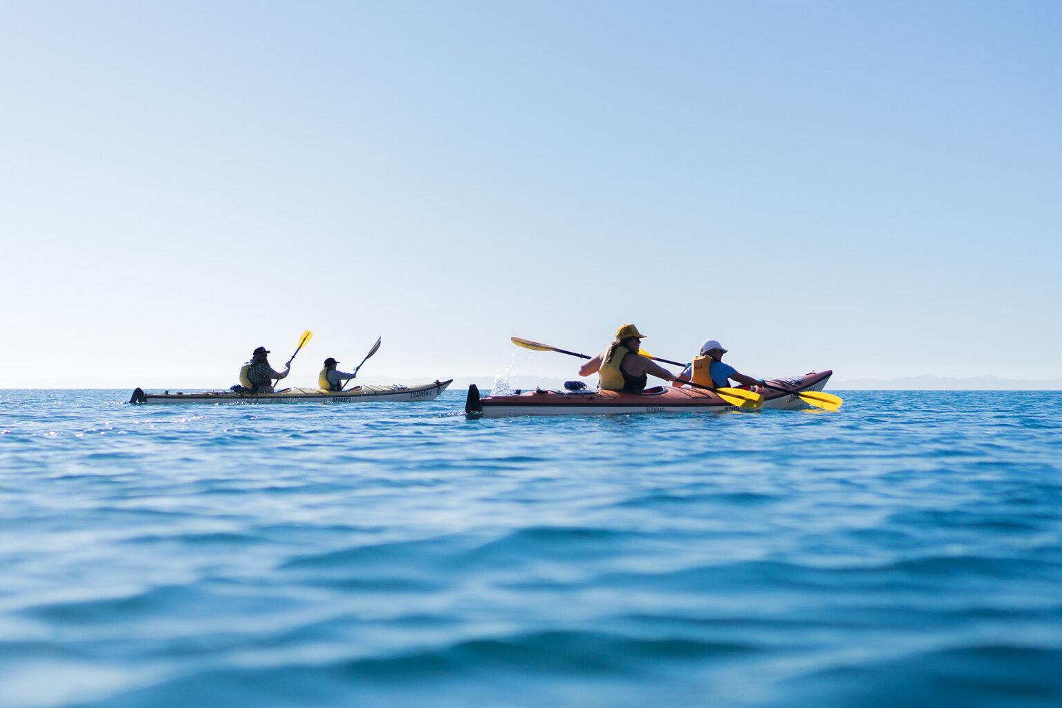 Two double-person sea kayaks are paddled by guests on turquoise blue water.