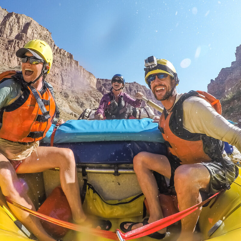 Three people in a yellow raft navigating the Colorado River through Cataract Canyon.