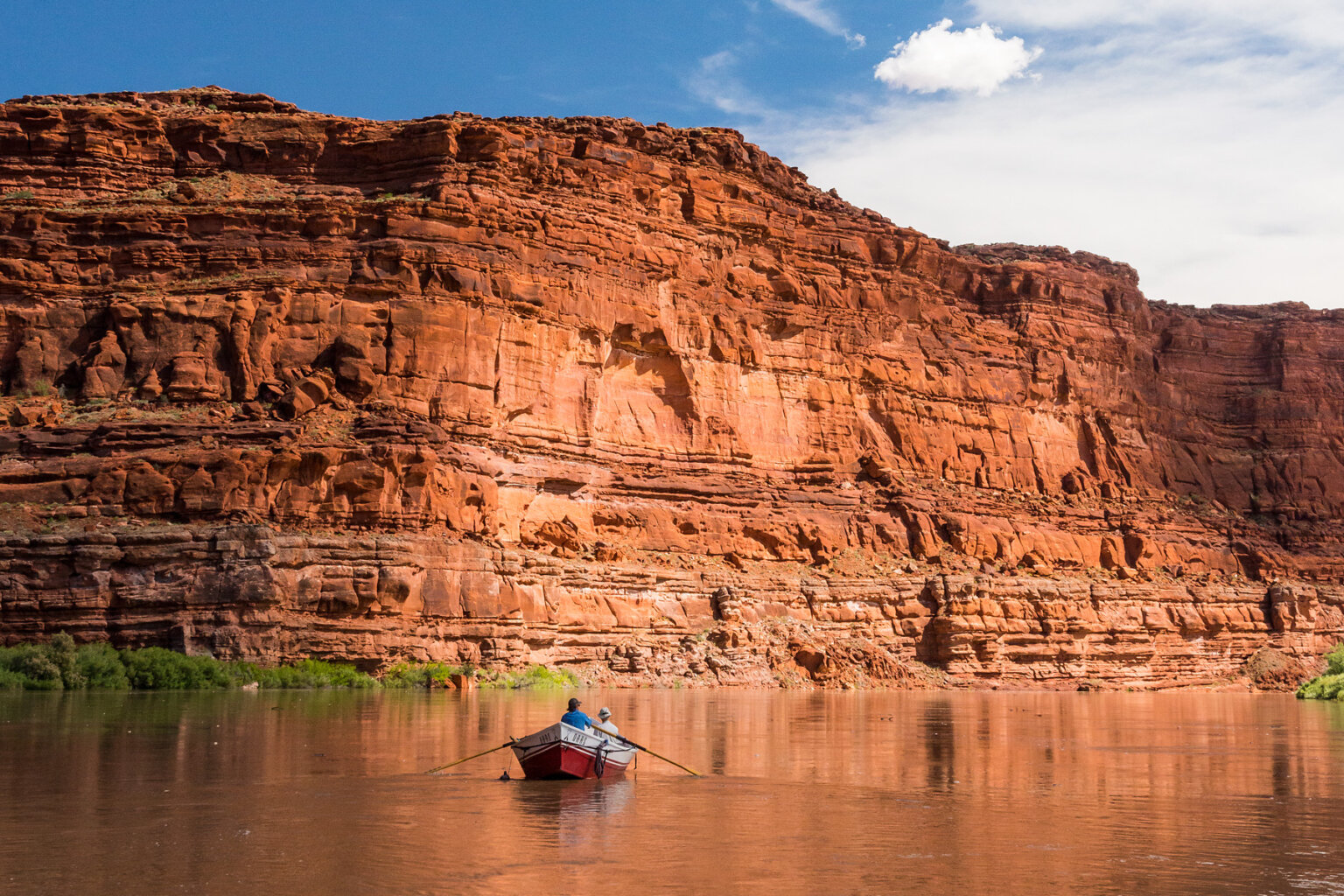 A dory rowing down the Colorado River in Cataract Canyon and giant redstone canyon walls rise around river.
