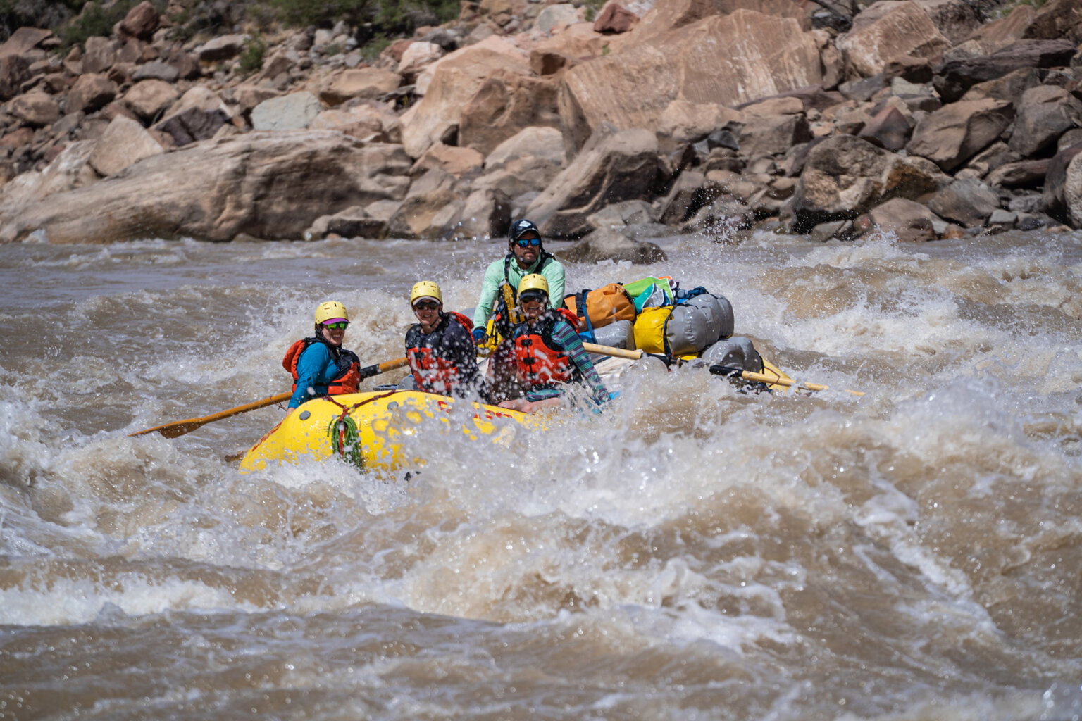 Three smiling rafters and a guide navigate through a stretch of whitewater on the Colorado River in Cataract Canyon.