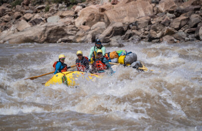Three smiling rafters and a guide navigate through a stretch of whitewater on the Colorado River in Cataract Canyon.