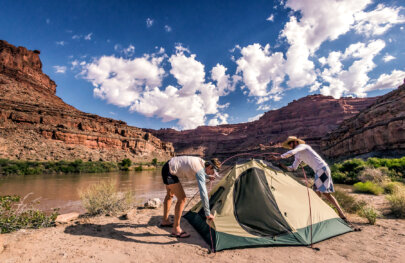 Two campers setting up a tent on the shore of the Colorado River on a Cataract Canyon rafting trip.