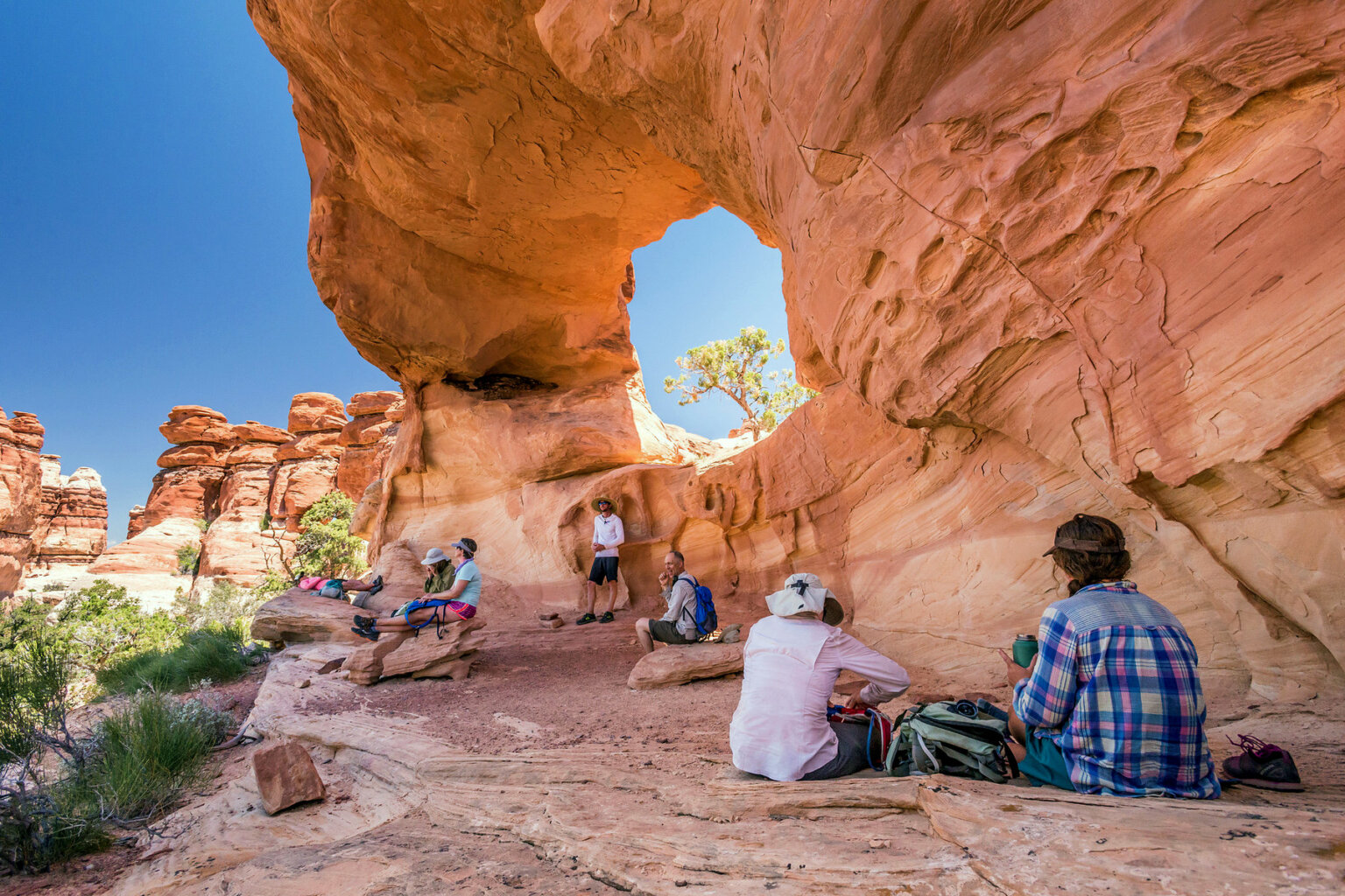 Several hikers relax in the shade of a massive arch on a hike in Canyonlands National Park.