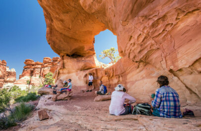 Several hikers relax in the shade of a massive arch on a hike in Canyonlands National Park.