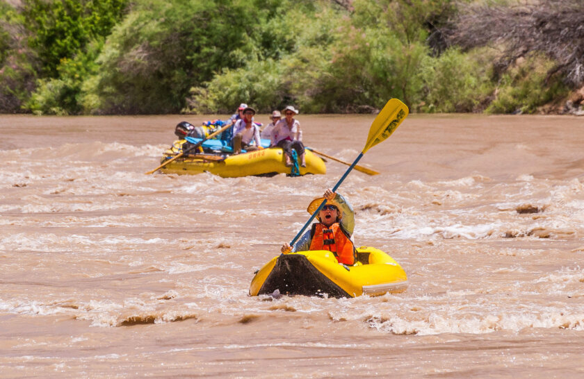 An excited kayaker paddles on the Colorado River while a raft of guests behind them watch.