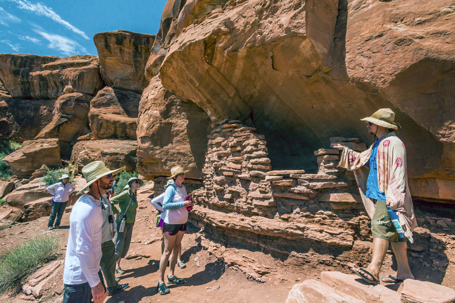 A guide draped in a sarong gives an interpretive talk while serveral guests listen at an archeological site in Canyonlands National Park.