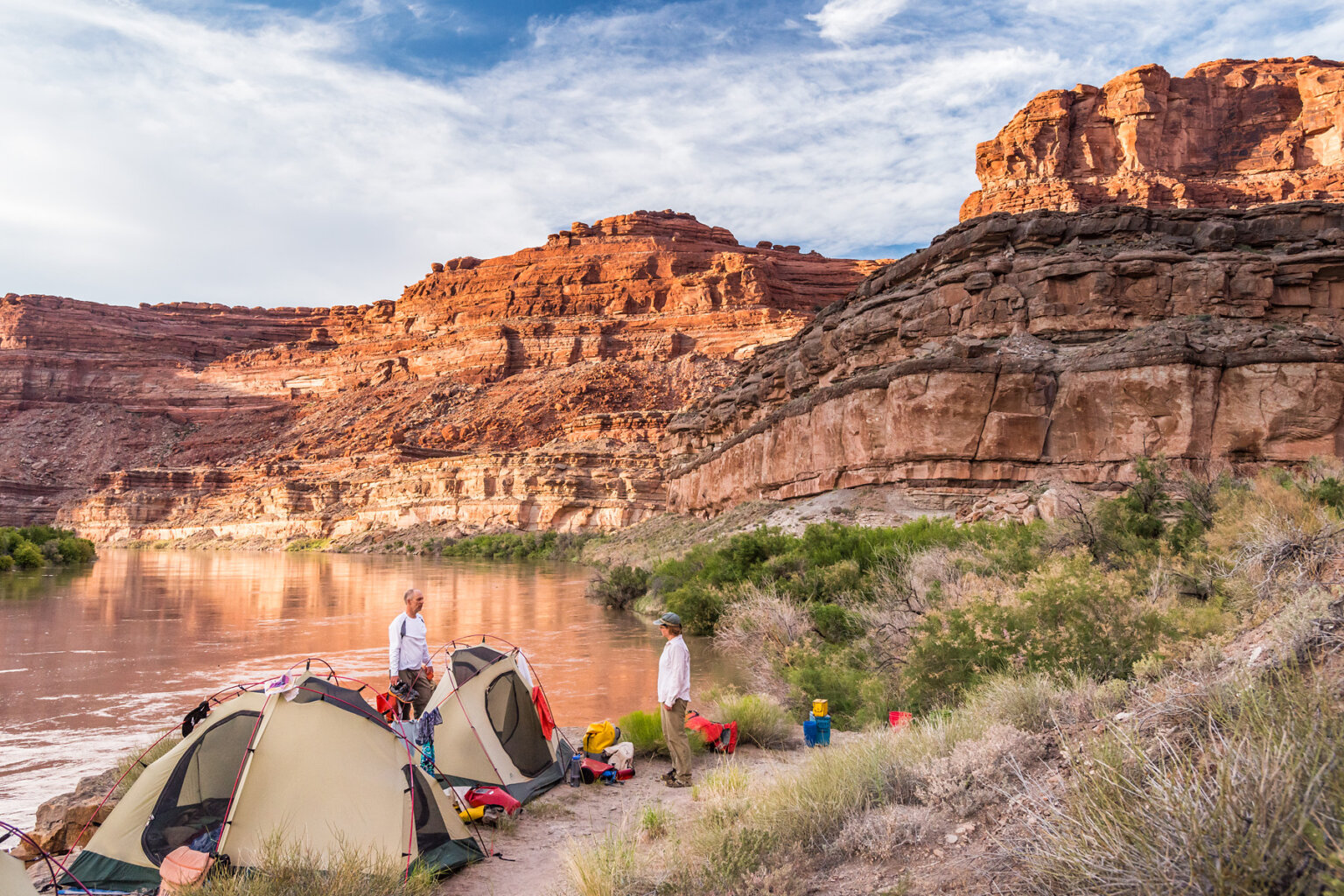 Two guests stand on the banks of the Colorado River near their tents at camp.
