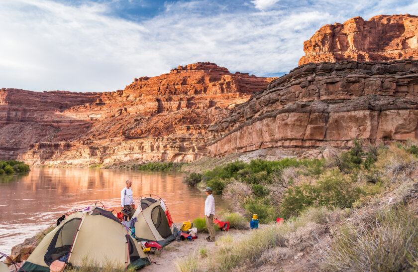 Two guests stand on the banks of the Colorado River near their tents at camp.