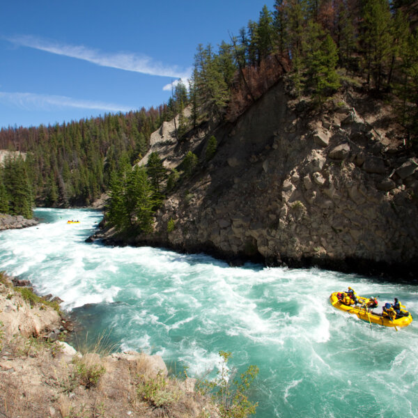 A yellow raft navigates a stretch of rapids on a turquoise blue river frothing with whitewater.