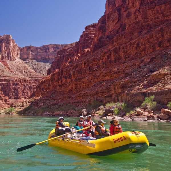 A yellow oar raft with people rowing down an emerald Colorado River in Grand Canyon