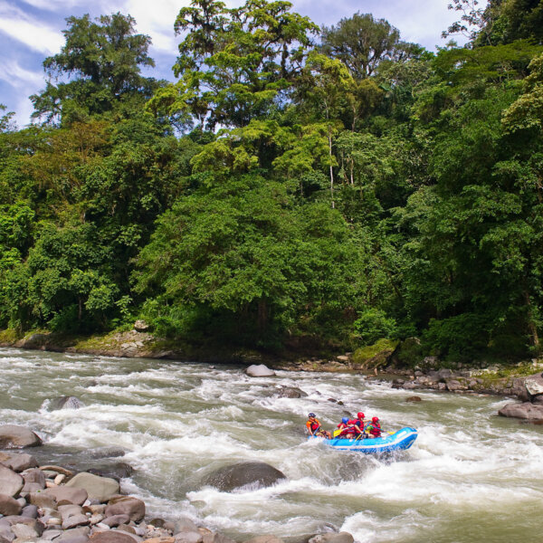 A paddle raft going through rapids surrounded by lush rainforest on a Costa Rica Pura Vida trip