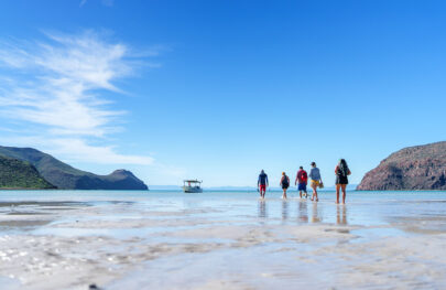 A group walks in shallow water off toward a boat in Baja, Mexico