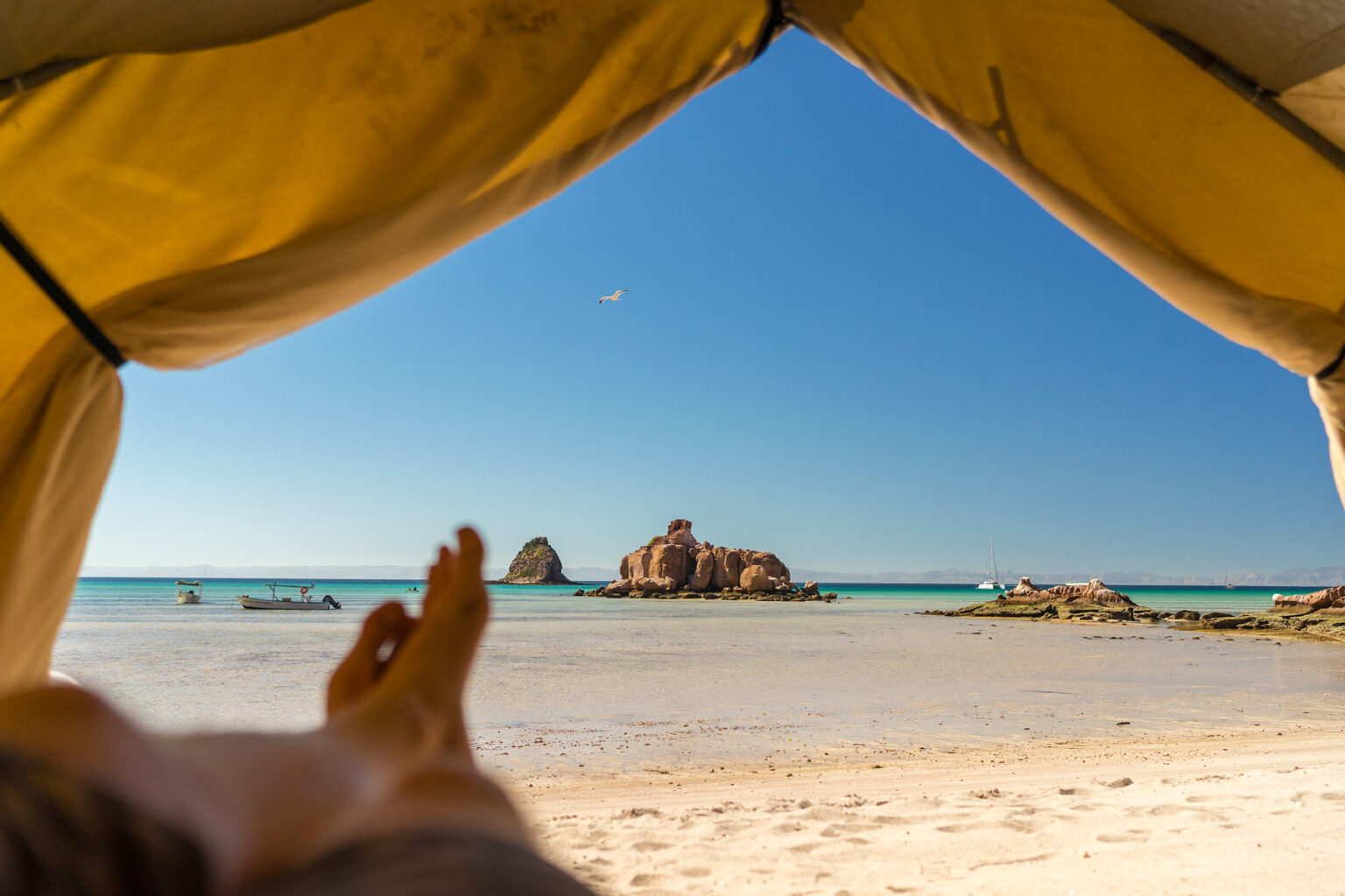 View of the ocean taken from inside a tent on a sandy beach in Baja Mexico as a guest kicks their feet up to relax