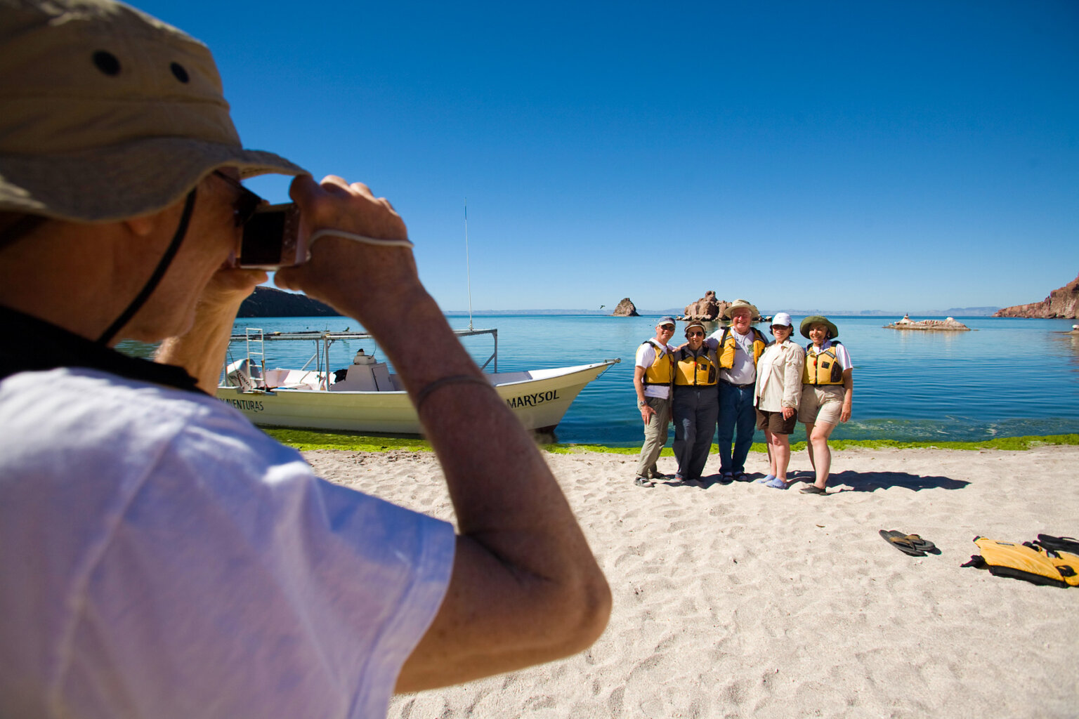 A group of guests stand on the beach with the ocean behind them as another guests takes their picture.