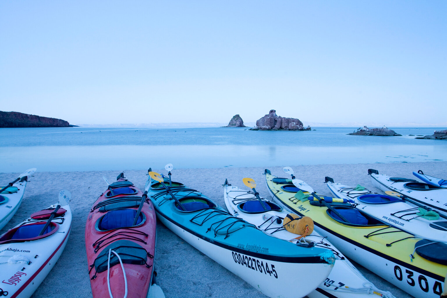 A row of sea kayaks pulled up on the beach with the ocean behind them in Baja Mexico.