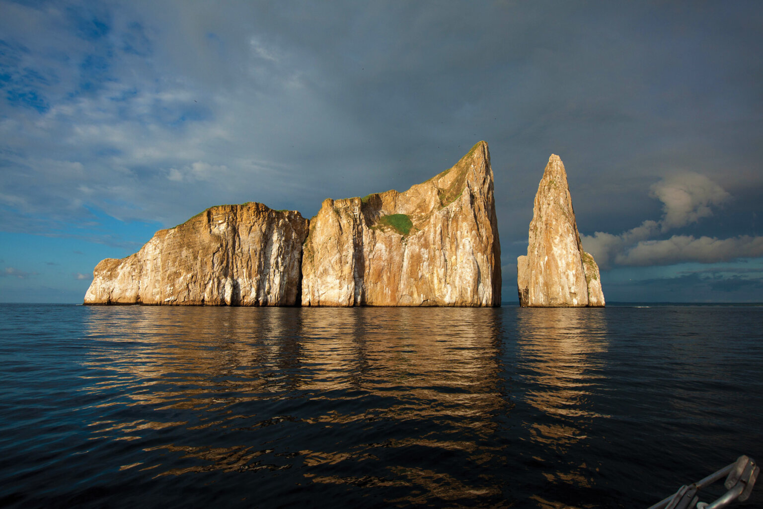 A large jagged rock formation rises out of the ocean as an island, lit up during magic hour in the Galapagos.