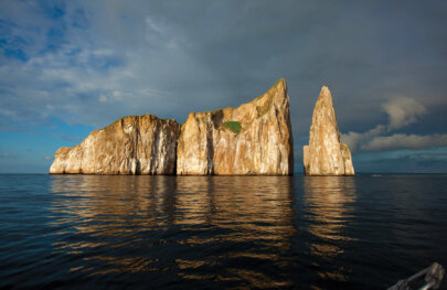 A large jagged rock formation rises out of the ocean as an island, lit up during magic hour in the Galapagos.