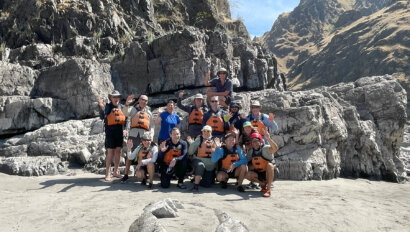 A group of people posing together outdoors in front of a rocky cliff under a clear blue sky.