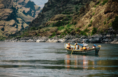 Four guests sit in a dory as a guide rows them down a calm section of the Snake River.