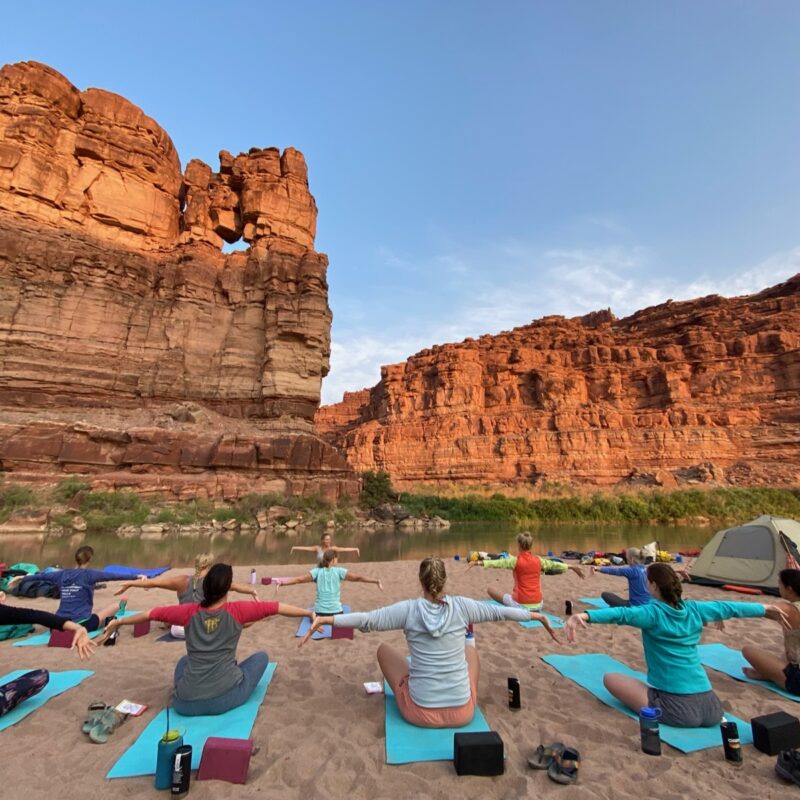 A group of women doing yoga on a sandy beach on an OARS Cataract Canyon Women's Wellness Retreat.
