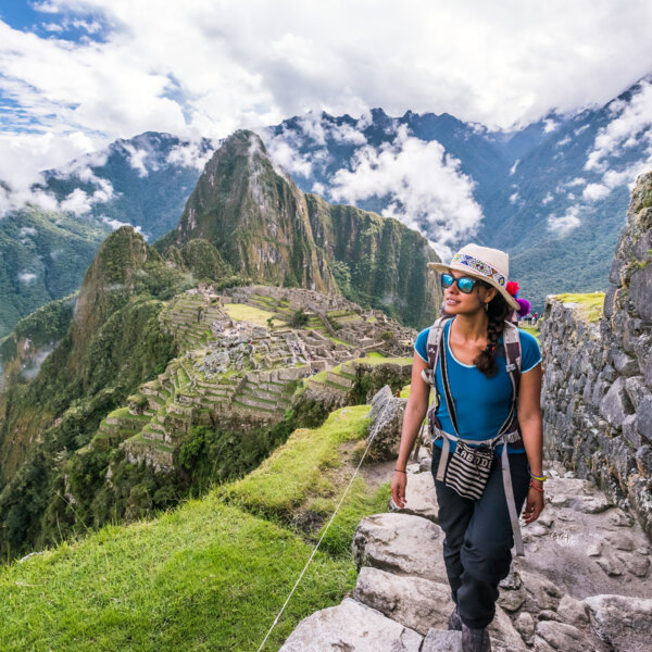 A woman wearing a traditional Peruvian hat hikes up rock steps high above Machu Picchu.