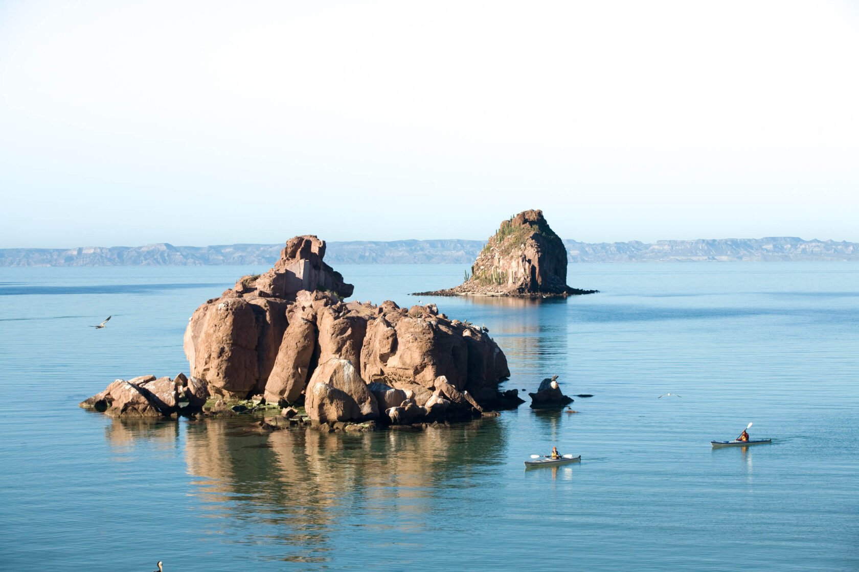 People kayaking next to big rocks in the ocean.