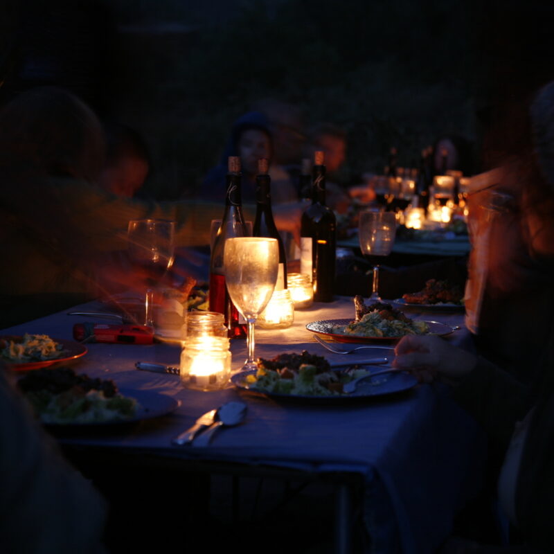 A group of people sit around a candlelit table enjoying a gourmet dinner on an OARS Rogue River Wilderness Gourmet trip.