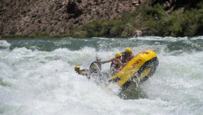 A small yellow raft with several passengers emerging from a massive whitewater wave in Lava Falls in Grand Canyon