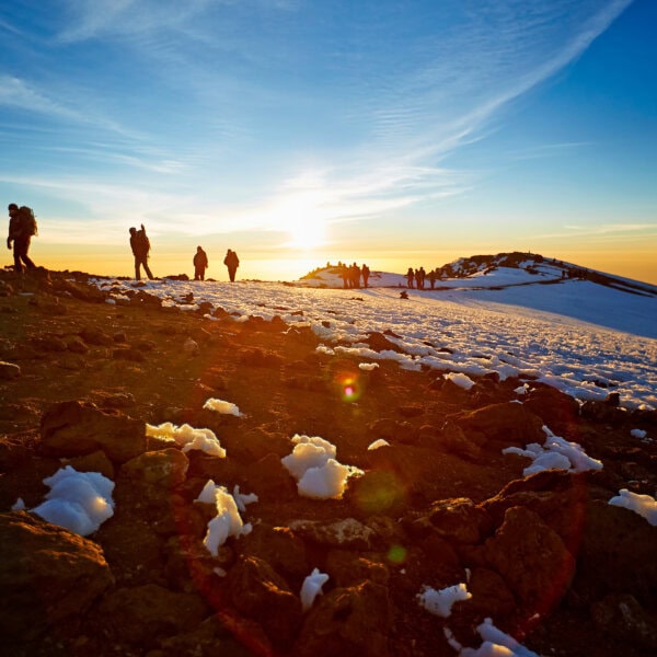 Hikers summit a snow-covered Kilimanjaro at sunrise