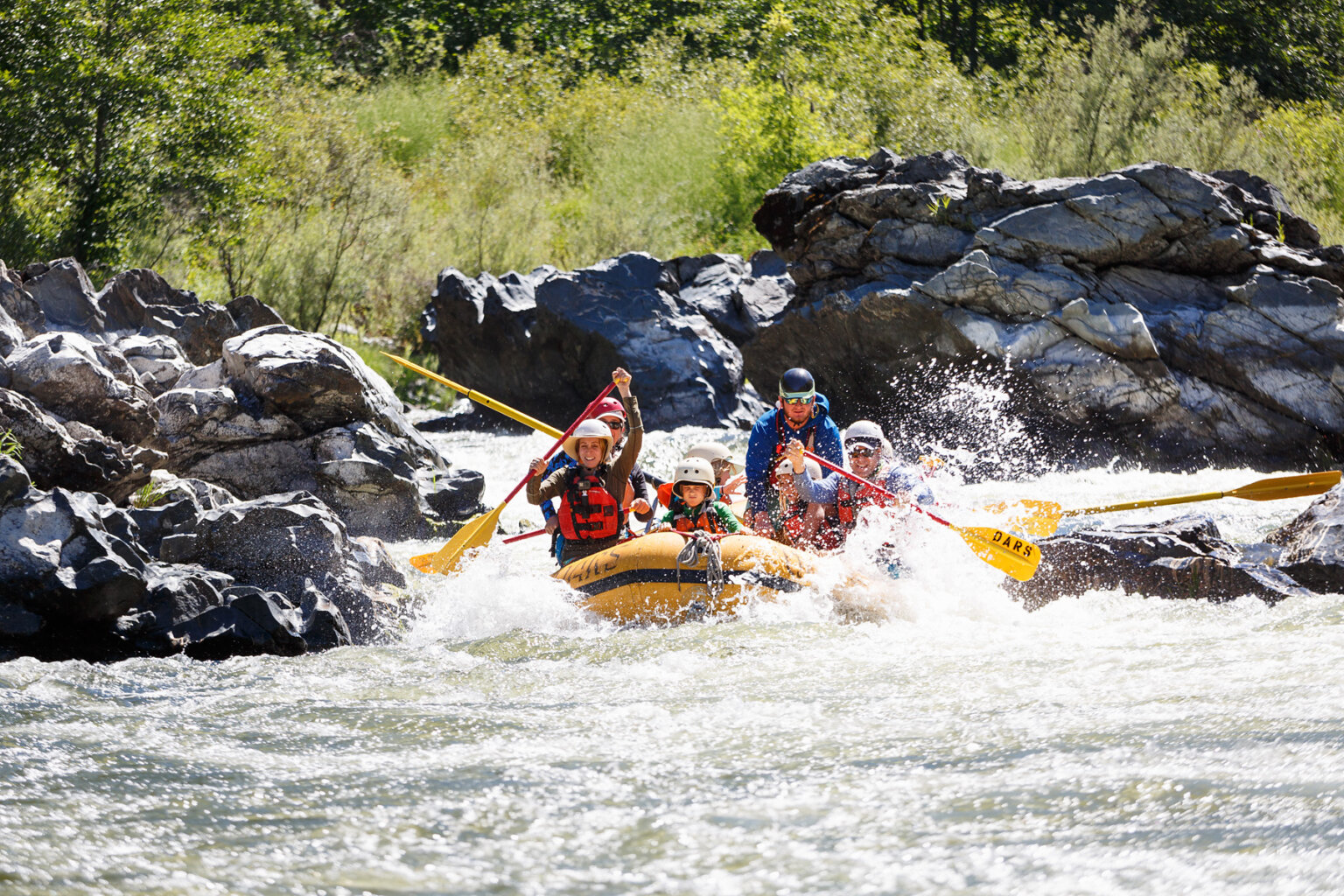 A kid sits in the very front of a yellow raft and holds on as adults behind him paddle through a rapid on the Lower Klamath River.