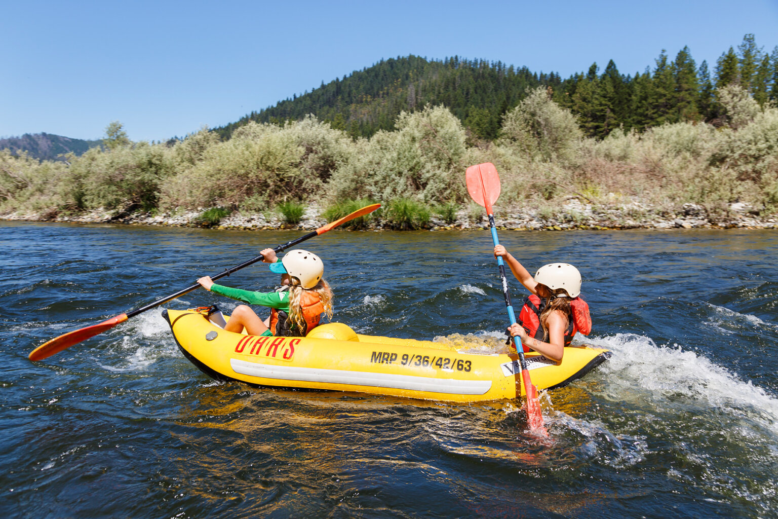 Side view of two young girls in a yellow inflatable kayak as they paddle downstream on the Lower Klamath River.