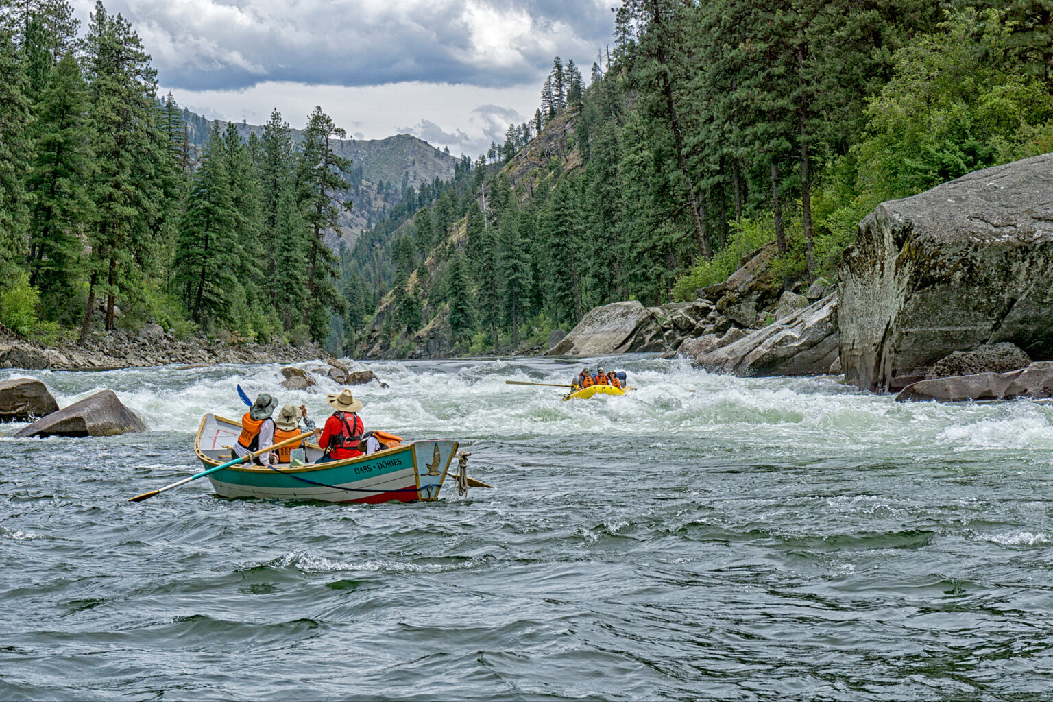 A dory full of people watches from below a rapid as an oar raft makes its way through the stretch of whitewater.