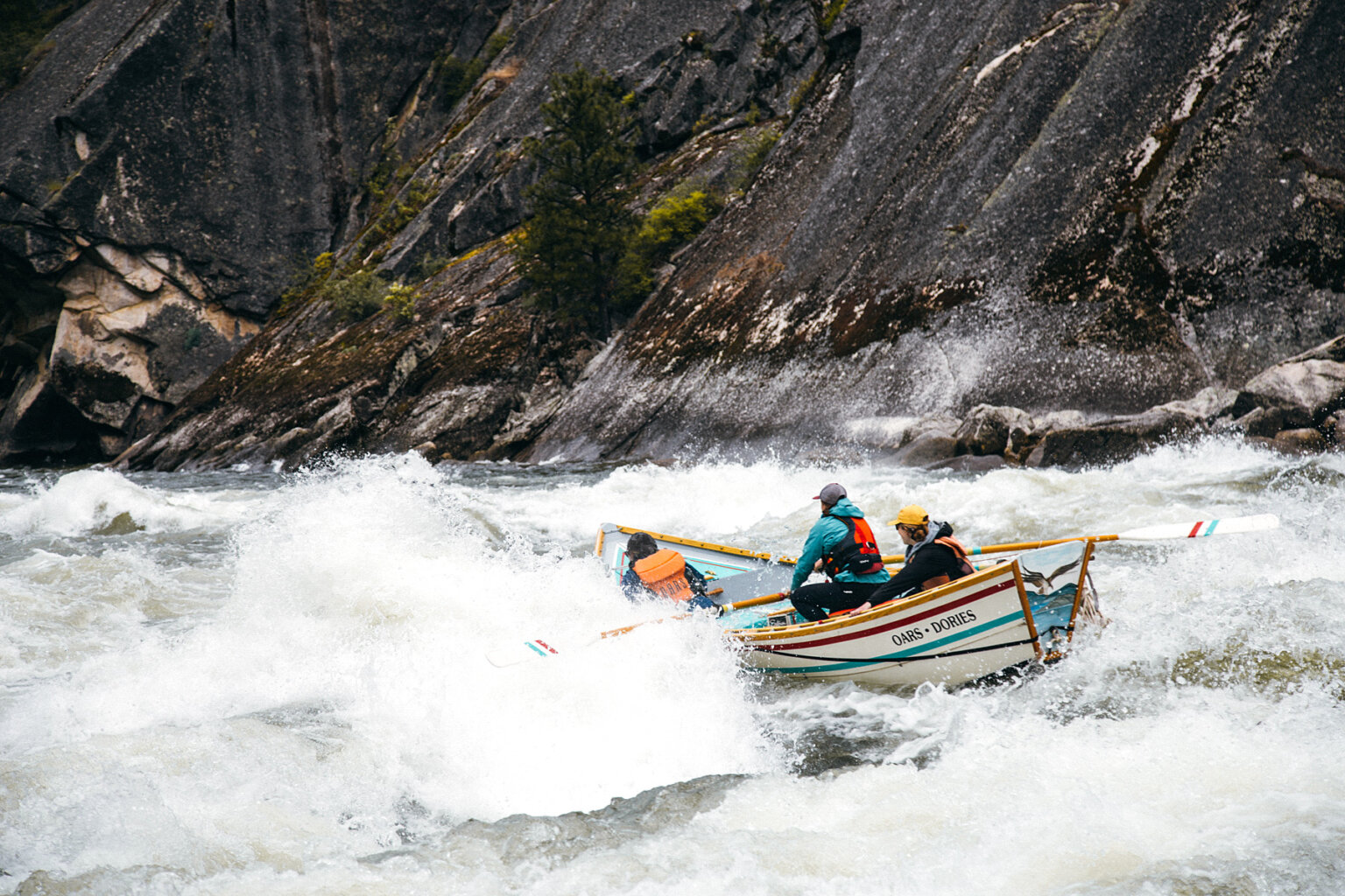 A dory with a guide and two guests plows through a big wave on a stretch of big whitewater on the Salmon River.