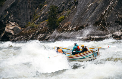 A dory with a guide and two guests plows through a big wave on a stretch of big whitewater on the Salmon River.