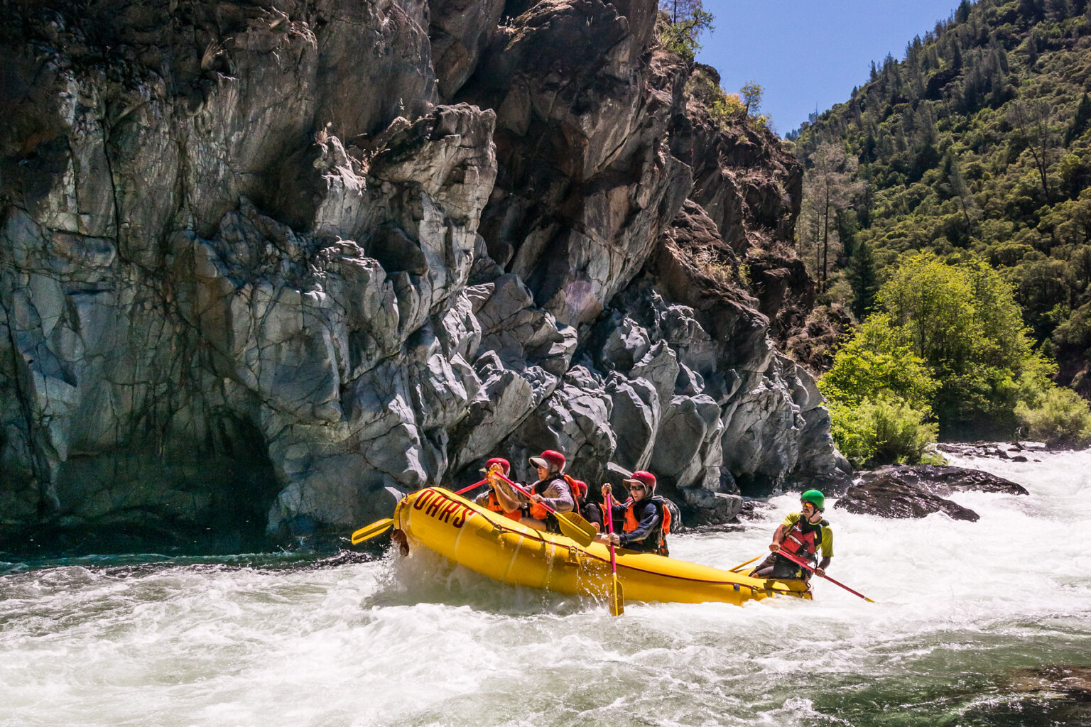 Side view of paddlers in a yellow raft with a guide in the back as they paddle through a stretch of whitewater on the Middle Fork American River.