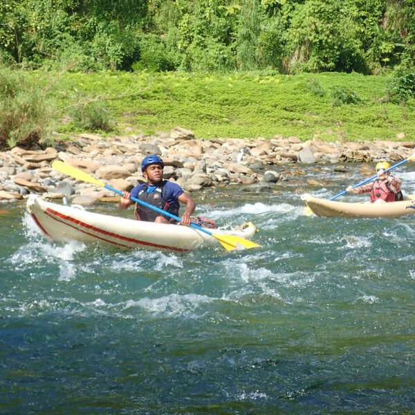 Guests in two inflatable kayaks paddle down the Middle Navua with green rainforest behind them.