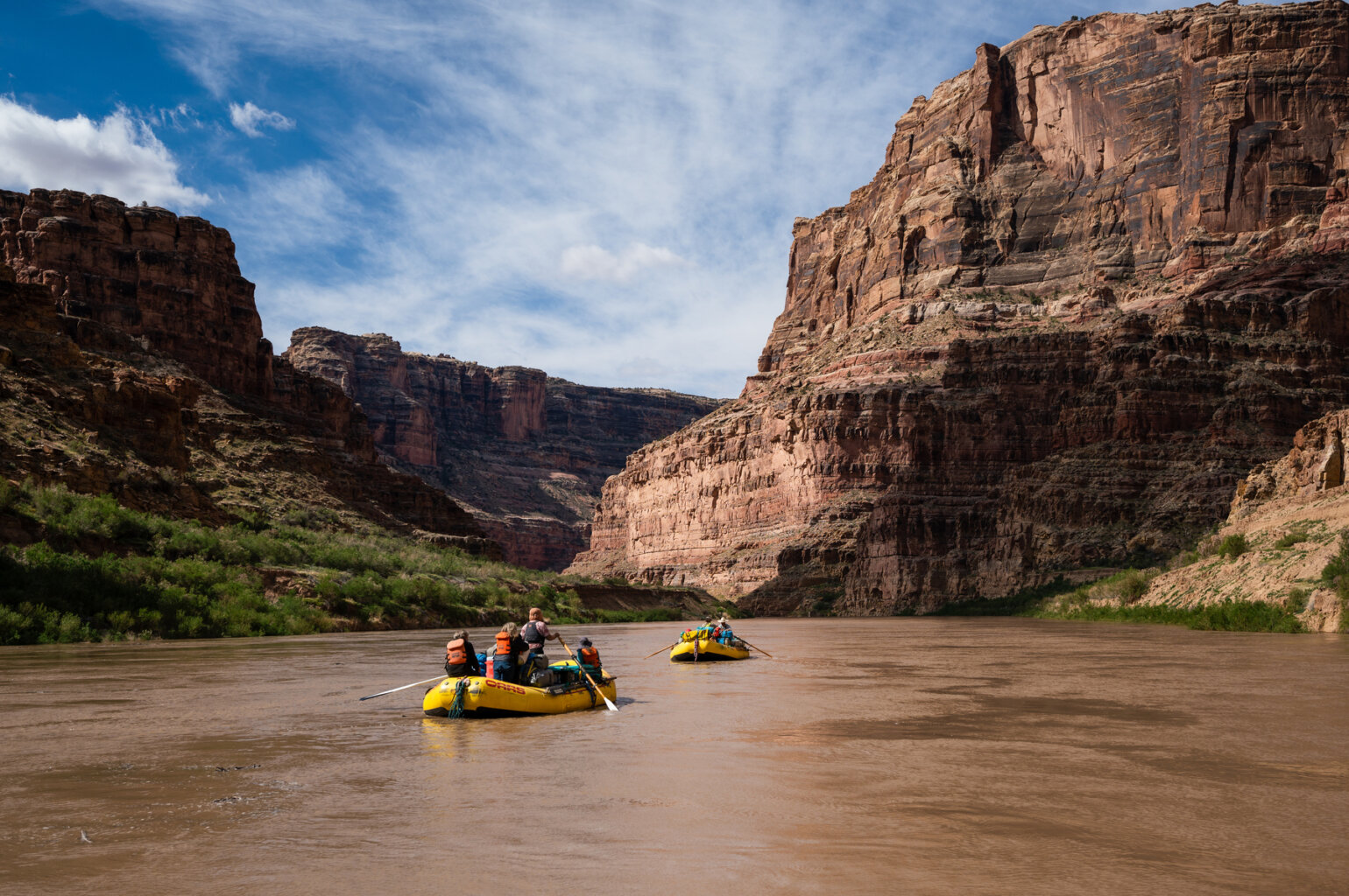 Two yellow rafts row down the Coloardo River with the large walls of Cataract Canyon surrounding them.