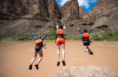 Three guests jump off a rock with their hands in the air into the Colorado River in Grand Canyon