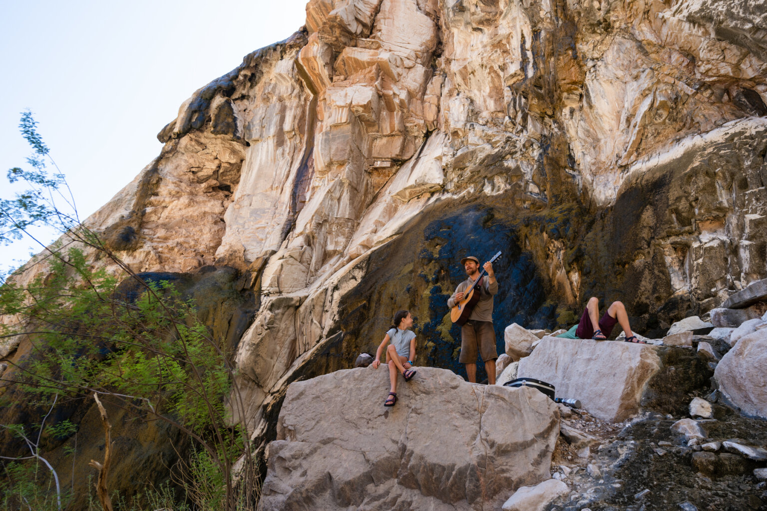 A guide plays guitar while a young girl watches and smile on a hike in Grand Canyon