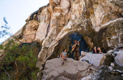 A guide plays guitar while a young girl watches and smile on a hike in Grand Canyon