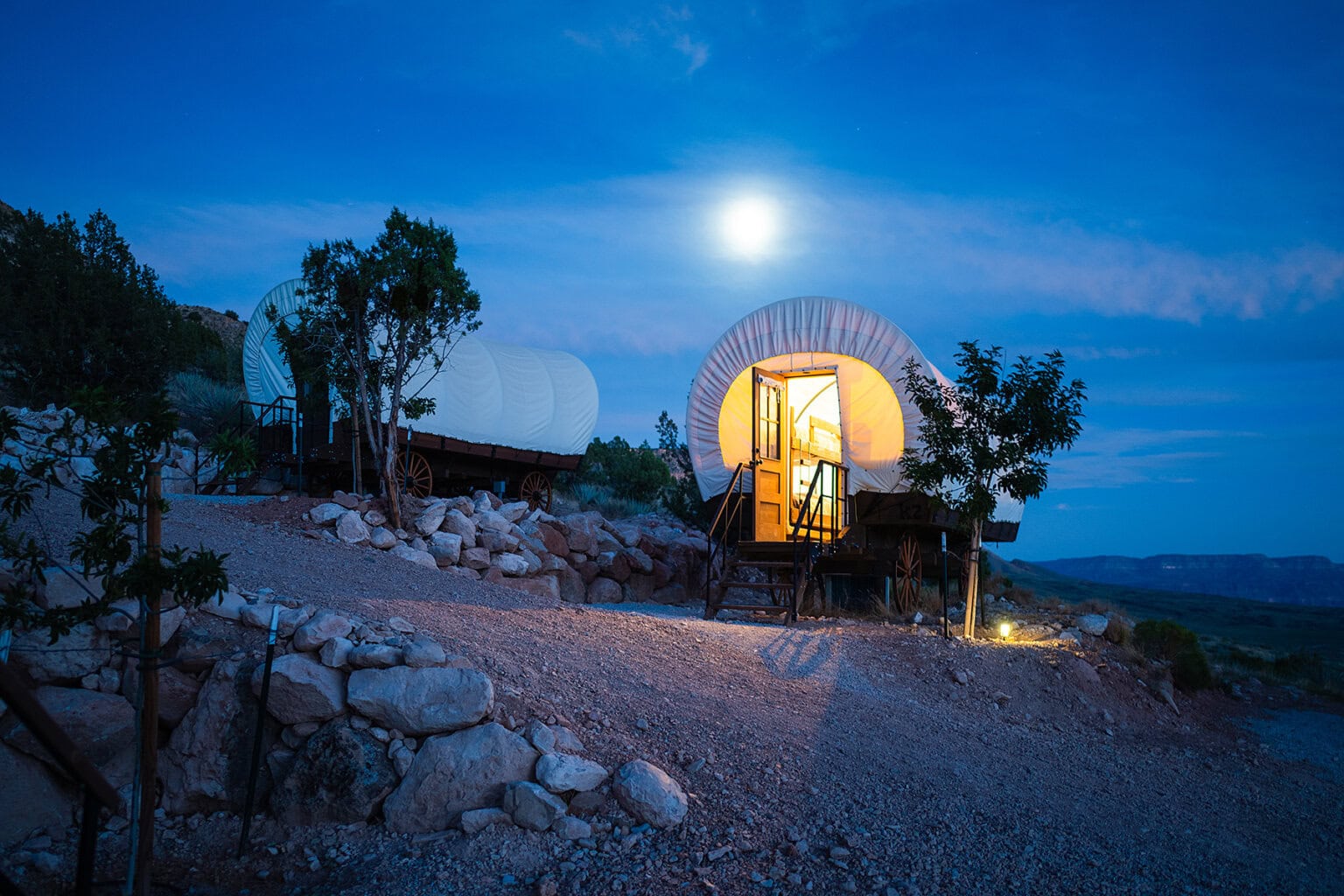A covered wagon glows illuminated from within beneath a full moon at Bar 10 Ranch