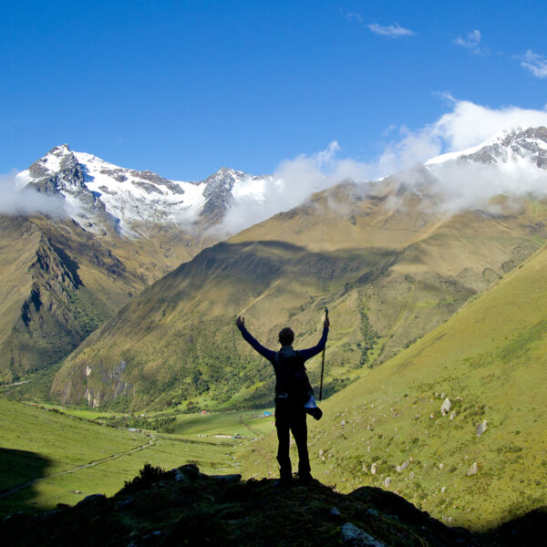 Silhouette of a guest on a vista with hands in the air overlooking green and snow-capped mountains in Peru.