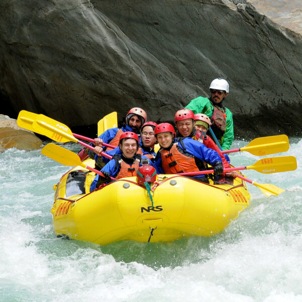 A group of guests holding paddles get down in a yellow raft as they go through a rapid on the North Fork American River.