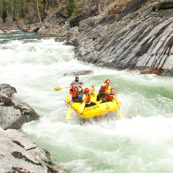 A paddle boat with four guets and a guide paddling through a large stretch of whitewater on the North Fork Stanislaus River.