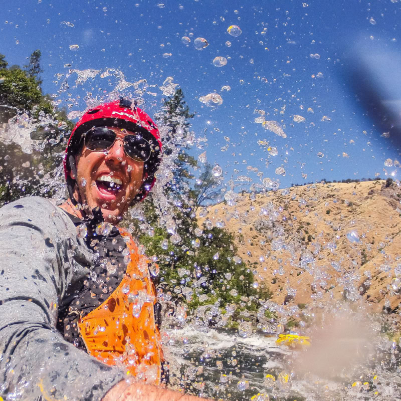 A laughing man getting splashed in the face by whitewater on the Tuolumne River in California.