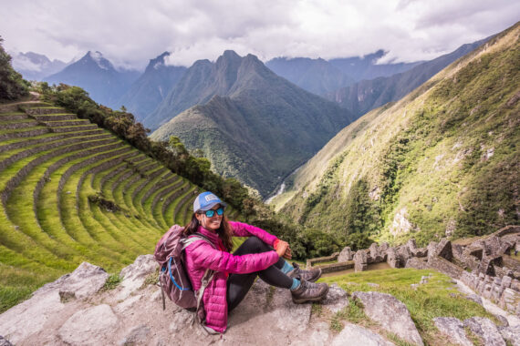A woman tourist sits above a view of terracing on the Inca Trail