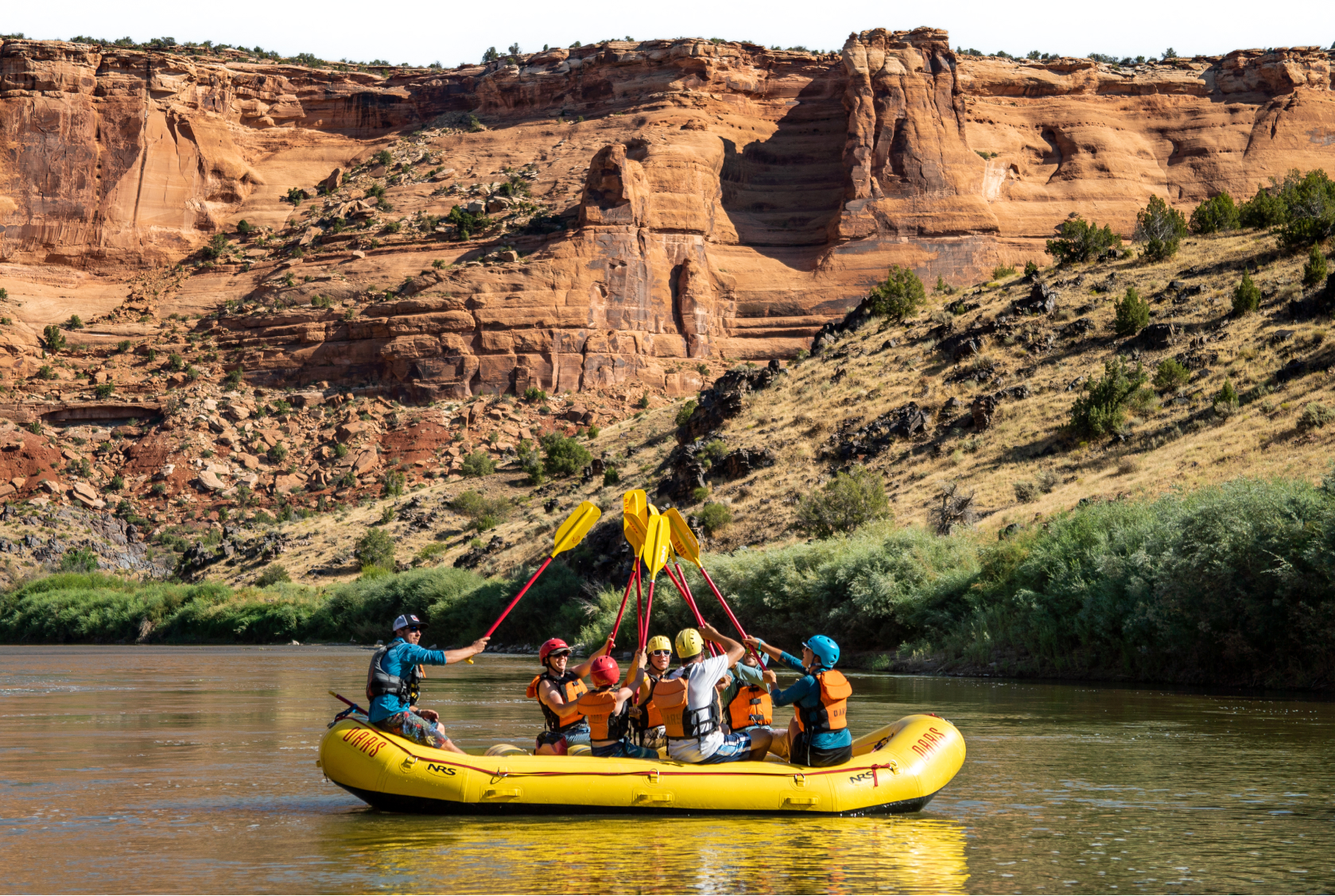 A group of paddlers in a yellow raft do a paddle high five on the river.