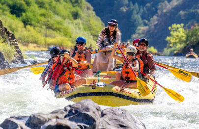 Guide qnd guests smile for the camera as they paddle their oar-assisted paddle raft through rapids on the Rogue River