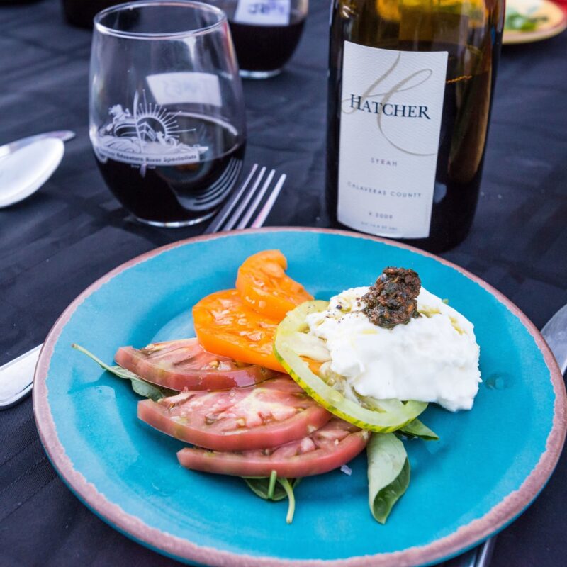 Close up on a gourmet tomato salad with a bottle of wine on a linen draped table on an OARS Wine on the River trip.